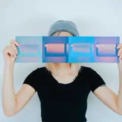 Osoba w czapce i czarnej koszulce trzyma przed twarzą panel z czterema prostokątami w odcieniach niebieskiego i różowego. Inspiracja do studiów artystycznych kierunki.