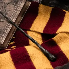 Magiczna różdżka i szalik w barwach Gryffindoru leżą obok ozdobnej księgi, idealne dla fanów szukających książek podobnych do Harrego Pottera.
