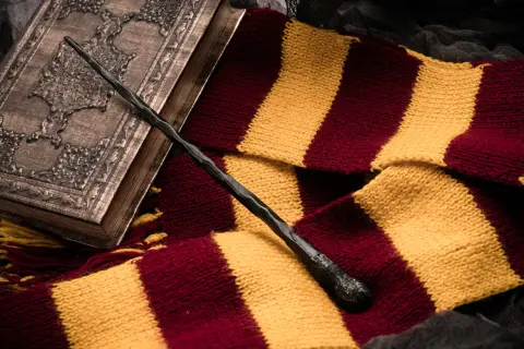 Magiczna różdżka i szalik w barwach Gryffindoru leżą obok ozdobnej księgi, idealne dla fanów szukających książek podobnych do Harrego Pottera.