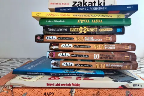 Stos książek o podróżach, w tym "Dookoła świata" i "Afryka Kazika", zachęca do odkrywania świata.