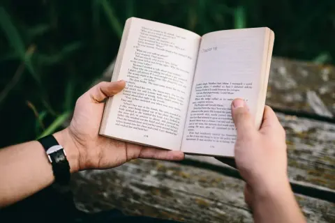 Ręce trzymają otwartą książkę z tekstem. To może być jedna z **książek sensacyjnych top 10**, idealna na relaksujący wieczór.